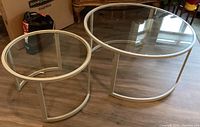 Top-down and angled view of two round glass nesting tables with silver metal frames on wood floor.