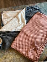 Two queen size throw blankets one dark grey with cream sherpa lining and one pink waffle textured blanket arranged on a carpeted floor.