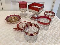 Full lot overview showing multiple vintage Tiffan-Franciscan Kings Crown glass pieces with red trim and gold accents including glasses, dishes and a candle holder on white textured surface.