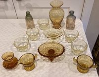 Wide shot showing all glassware pieces including large amber vase, small bowls, ribbed vases, drinking cups, and serving bowls.