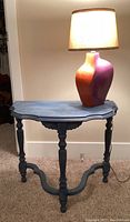 Front view of blue wooden table with ornate carved detailing and colorful ceramic lamp on top with lampshade on