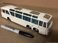 Side and top view of white die-cast model bus with clear roof panels and blue interior seats, shown next to Sharpie marker for size scale.