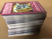 Side view of a thick stack of Yu-Gi-Oh! cards showing the card edges with various colored borders typical of monster, spell, and trap cards.