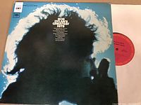 Vinyl LP record partially shown out of the original album cover featuring Bob Dylan's Greatest Hits with profile image of Bob Dylan in silhouette.