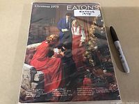 Front cover of Eaton's Christmas 1975 catalog showing a family scene with a decorated Christmas tree and period clothing, alongside a black marker pen for size reference.