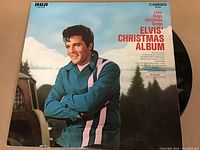 Front cover photo of Elvis Presley 'Elvis' Christmas Album' LP with Elvis posing in winter clothes next to a snowy scene. Vinyl partially visible in sleeve.