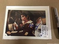 Photo of the oversized photo card showing Kirstie Alley in Star Trek II: Wrath of Khan costume, holding a communicator and signed in blue ink.