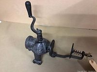 Full side view of the cast iron coffee grinder showing the crank handle, body with embossed decoration, and clamp base.