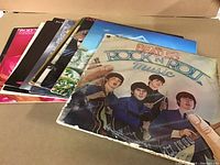 Photo showing an array of LP records including Beatles 'Rock 'N' Roll Music' album with visible edge wear and some discoloration, along with other LP records stacked behind.
