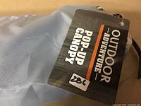 Close-up of the carry bag tag showing 'Outdoor Adventure Pop-Up Canopy' branding.