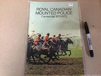 Front cover of the Royal Canadian Mounted Police Centennial book showing officers on horseback with lances, a Sharpie marker for scale.