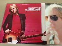 The album cover of the Tom Petty and the Heartbreakers vinyl LP showing the artist holding a guitar with a red background and a close-up side photo of Tom Petty wearing sunglasses.