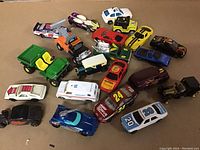 Photo showing 18 different toy diecast vehicles including cars, trucks, ambulance, police car and tractor in varying colors and styles on a brown background.
