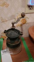 Overview of antique hand cranked coffee grinder showing cast iron body and glass base with wear and patina.