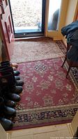 View of two carpets on floor near entrance door - larger red carpet with floral patterns and smaller beige carpet seen on top.
