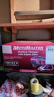 Box of Motomaster battery charger with engine start, clear product labeling and specifications, placed in storage area.