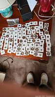 Overview of over 100 assorted coins from different countries spread out on table with some coins in plastic bag and black box nearby.