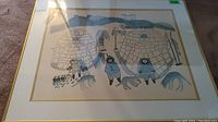 Full view of framed Inuit print showing igloos, figures, sled dogs, and landscape in blue tones.