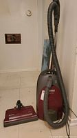 Full view of red Kenmore Whispertone vacuum with grey hose and separate power head on floor.