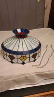Full view of stained glass lamp shade showing white, blue, yellow, and brown glass pieces with decorative top finial