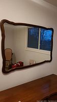 Full view of vintage wall mirror with wood frame hung on a wall, showing rectangular shape with curved edges and reflective mirror glass.