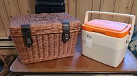 Wicker picnic basket and Coleman cooler side by side on metal folding table