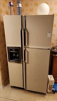 Beige Inglis Royal 100 refrigerator exterior with side-by-side doors and water dispenser on freezer door, shown against a wallpapered wall.