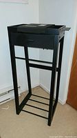 Full view of lightweight black standing valet with 4 legs and rectangular top surface