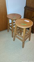 Two light-colored wooden stools with round seats side by side, showing general view and condition