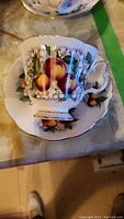 Close-up of a tea cup and matching saucer featuring a fruit and floral design with gold trim.