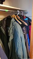Coats hanging in closet showing various colors and styles, including green padded coats and other winter jackets.