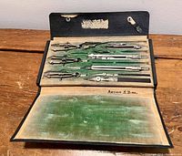 Image showing the inside of the opened black case with felt lining, containing metal drafting compasses and dividers, signed Arthur S. Bird.