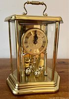 Front view of brass Bulova carriage clock with Roman numeral dial and rotating pendulum inside glass case.