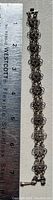 Full length photo of the silver filigree bracelet next to a ruler showing it measures about 7 inches.