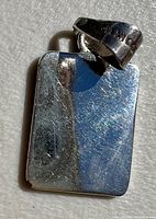 Close-up image showing the engraved mark '925 Mexico' on the bail and the smooth flat back surface of the rectangular sterling silver pendant with surface scratches visible.