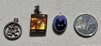 Lot of three silver pendants next to a coin for size reference. Pendants include circular cat design, rectangular resin piece, and oval painted cat.