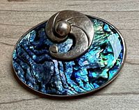 Close-up photo showing vibrant blue and green abalone shell with Sterling silver abstract spiral design on top.