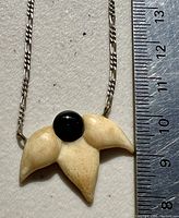 Close-up of the pendant showing the carved bone with a black center on a sterling silver link chain and a measuring ruler beside showing size.