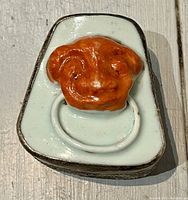 Top down view showing the white porcelain lid with an orange-brown Fu Dog (Foo Dog) head and a white ring handle.