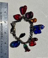 Full view of the charm bracelet with ruler for size reference showing various colorful glass charms on the chain.