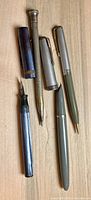 Overview photo of the four pens and pencils showing various colors and finishes including blue marbled, silver metal, light gray, and green items.
