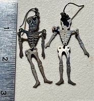 Pair of articulated sterling silver skeleton earrings lying next to a ruler showing about 2.5 inch length each.