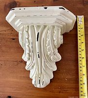 Front view of the white distressed ornate wall sconce shelf with measuring tape showing about 7.5 inch height.