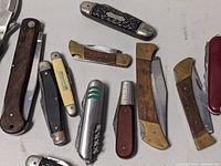 Overview of all 12 vintage pocket knives displayed on a flat surface, showing variances in handle materials and sizes.