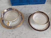 Shows two full sets of cups and saucers side by side, illustrating different patterns and colors, highlighting gold trims and white porcelain base.