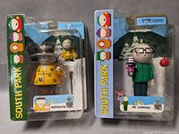 Full view of both Mephesto and Mr. Garrison figures in sealed blister packaging against a grey background.