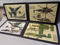 Photo showing four large laminated military aircraft prints arranged on a table showcasing multiple aircraft illustrations and detailed descriptions.