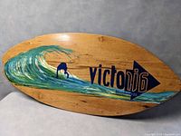 Front view of the wooden skimboard showing wave and surfer design and Victory logo.