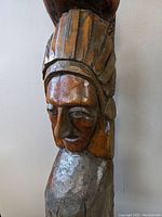 Close-up of carved indigenous face on the totem pole with feathered headdress details.