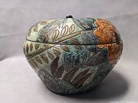 Side view of the apple-shaped Chinese ceramic jar displaying floral and leaf motifs with a lid and small black stem on top.